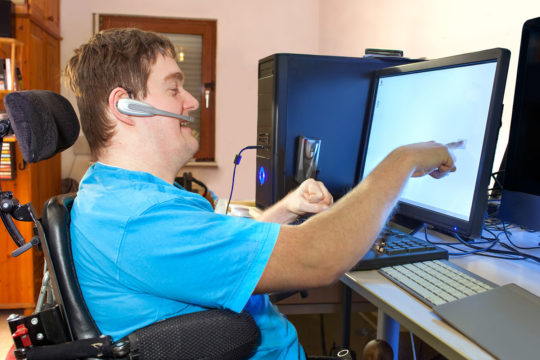 a young man with cerebral palsy sitting using touch screen computer