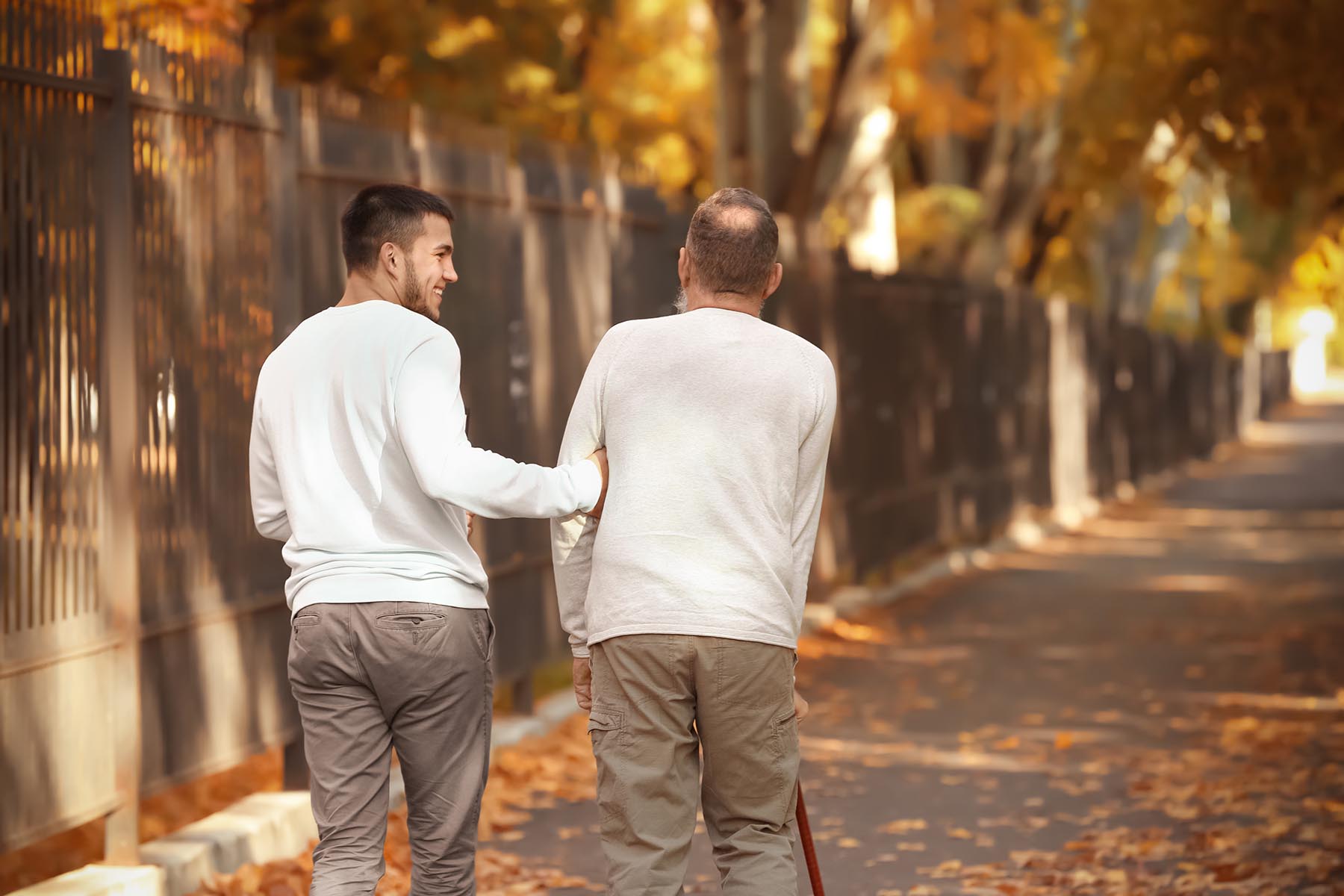Young caregiver walking with senior man in park