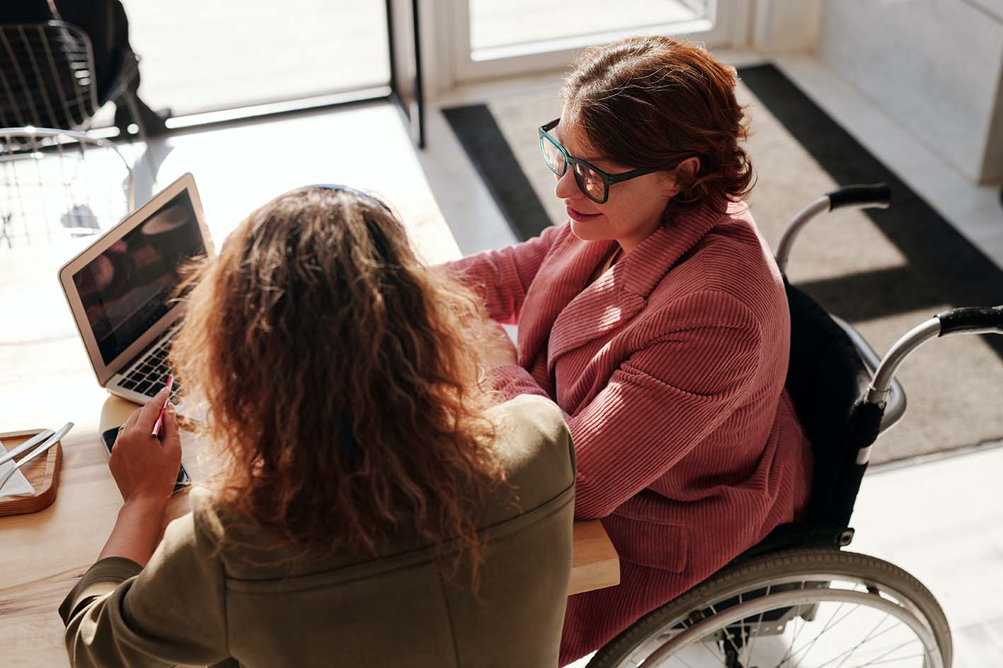 Person in wheelchair looking at laptop with friend. Photo by Marcus Aurelius
