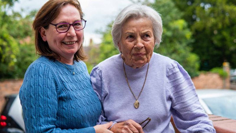 smiling middle aged person helping older person to stand upright