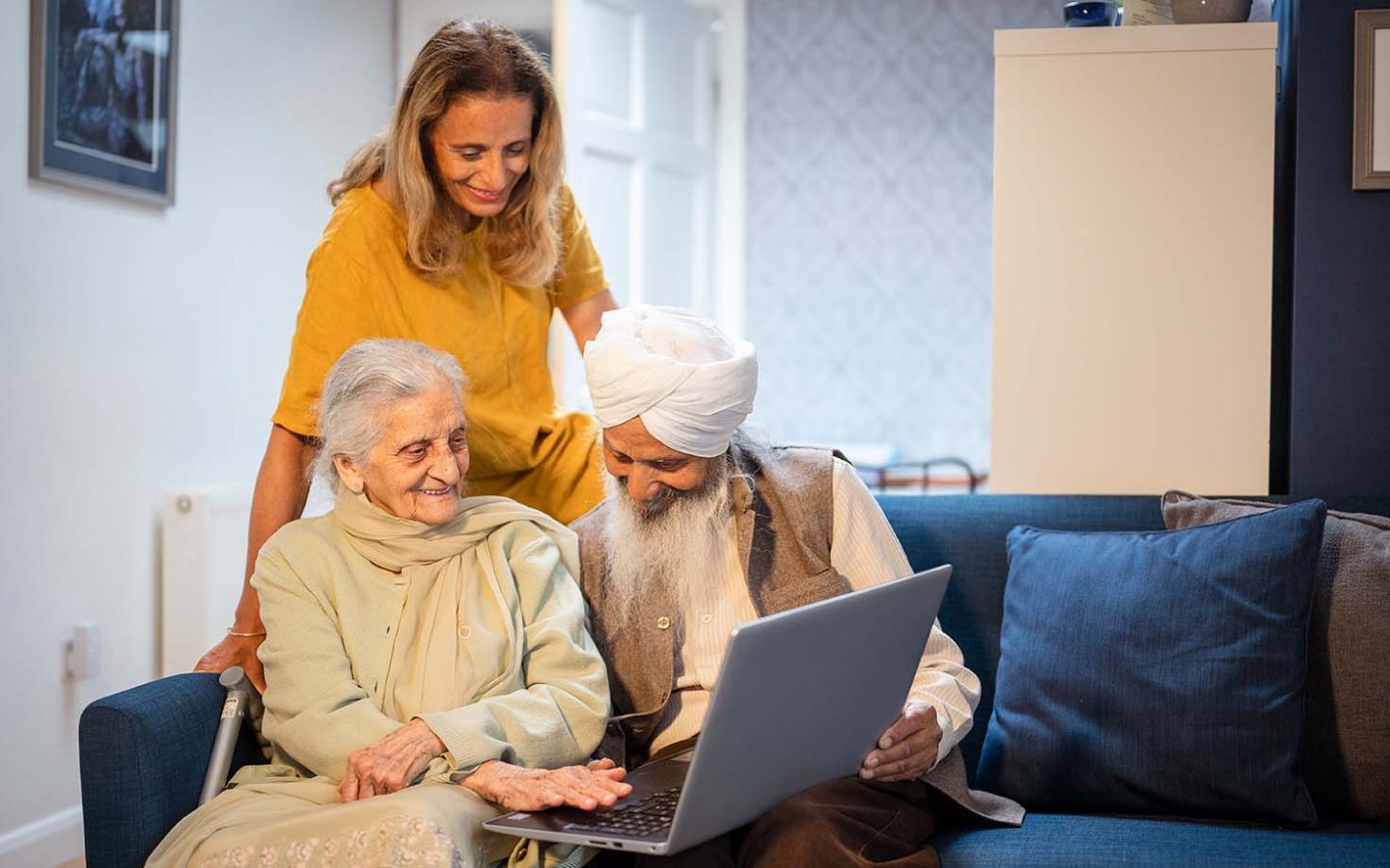 Older couple using laptop, younger female supervising, all smiling. CREDIT: Peter Kindersley