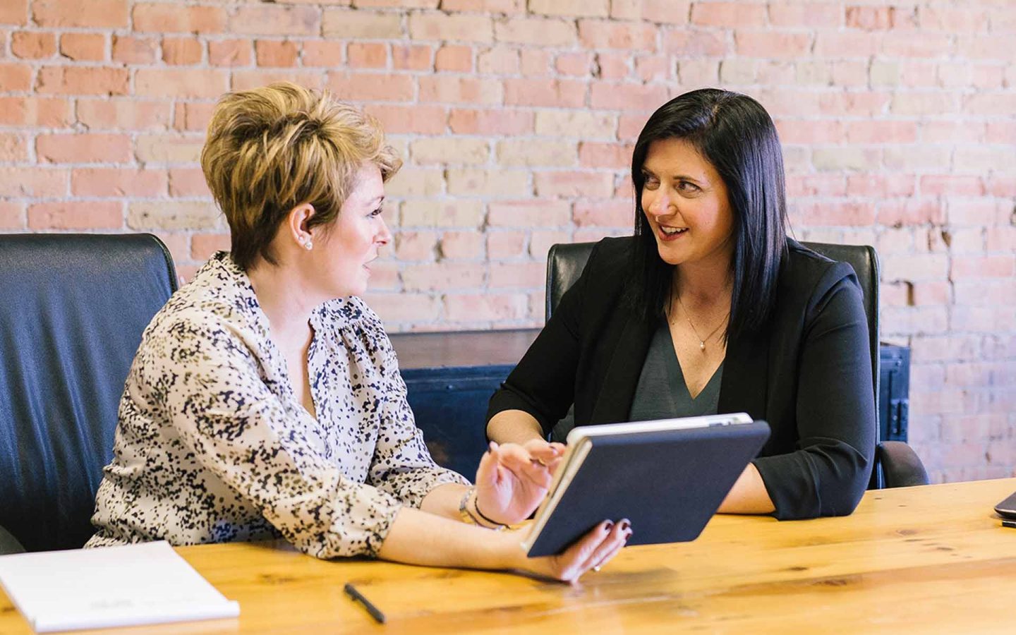 two people talking with a tablet device and pad of paper nearby